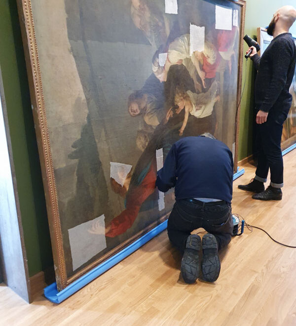 Deux hommes posent du papier japon sur la peinture de jean-Benoit Suvee, représentant Jésus
