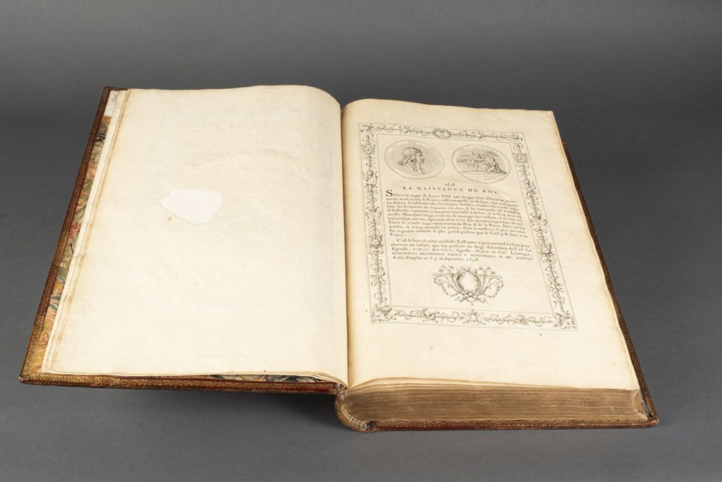Manuscrit ouvert avec une gravure de la médaille de Mollart représentant « La naissance du Roy » sur les deux faces